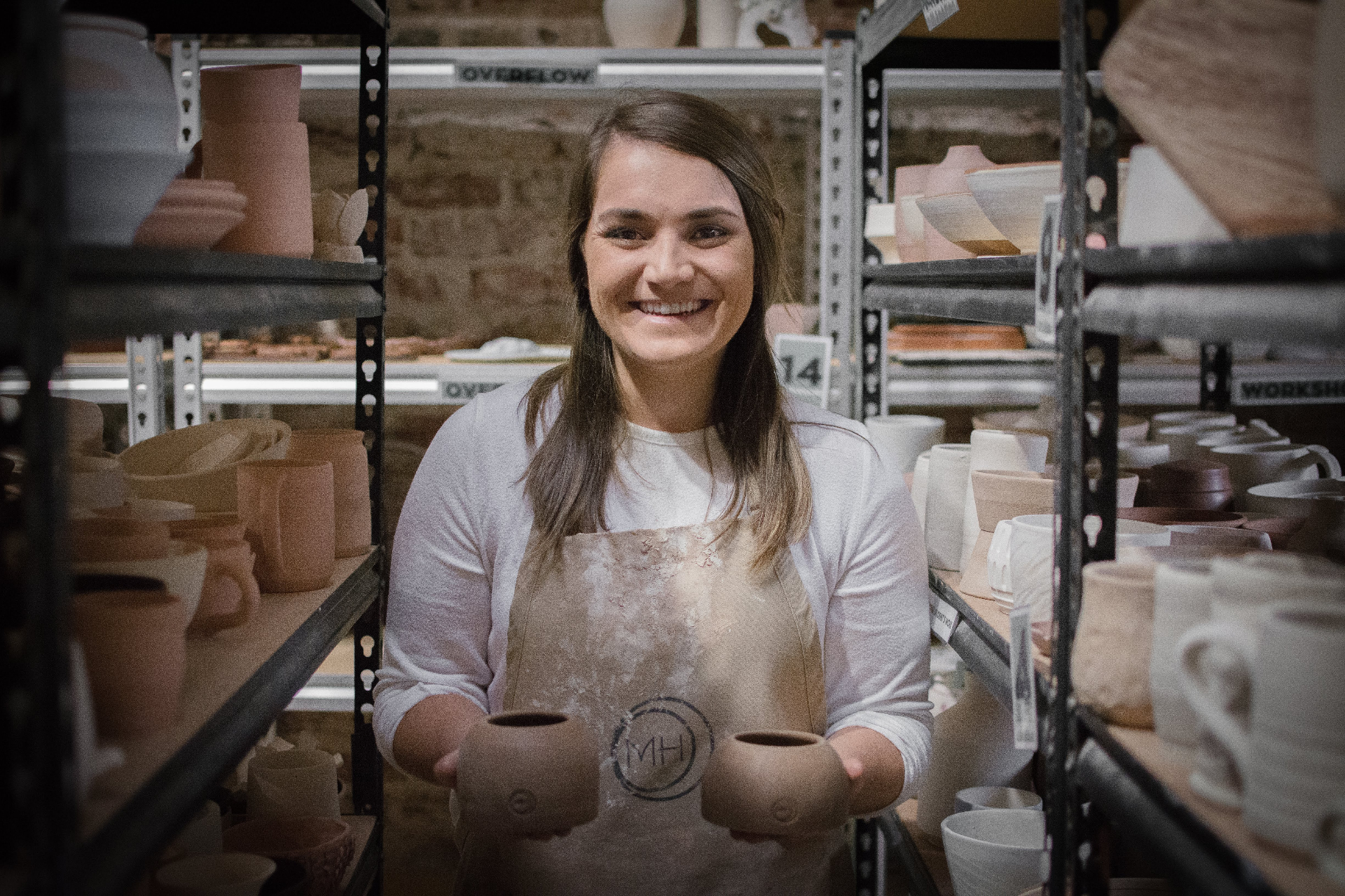 Muds founder smiling in the studio holding two freshly thrown vessels stamped with the MH maker's mark