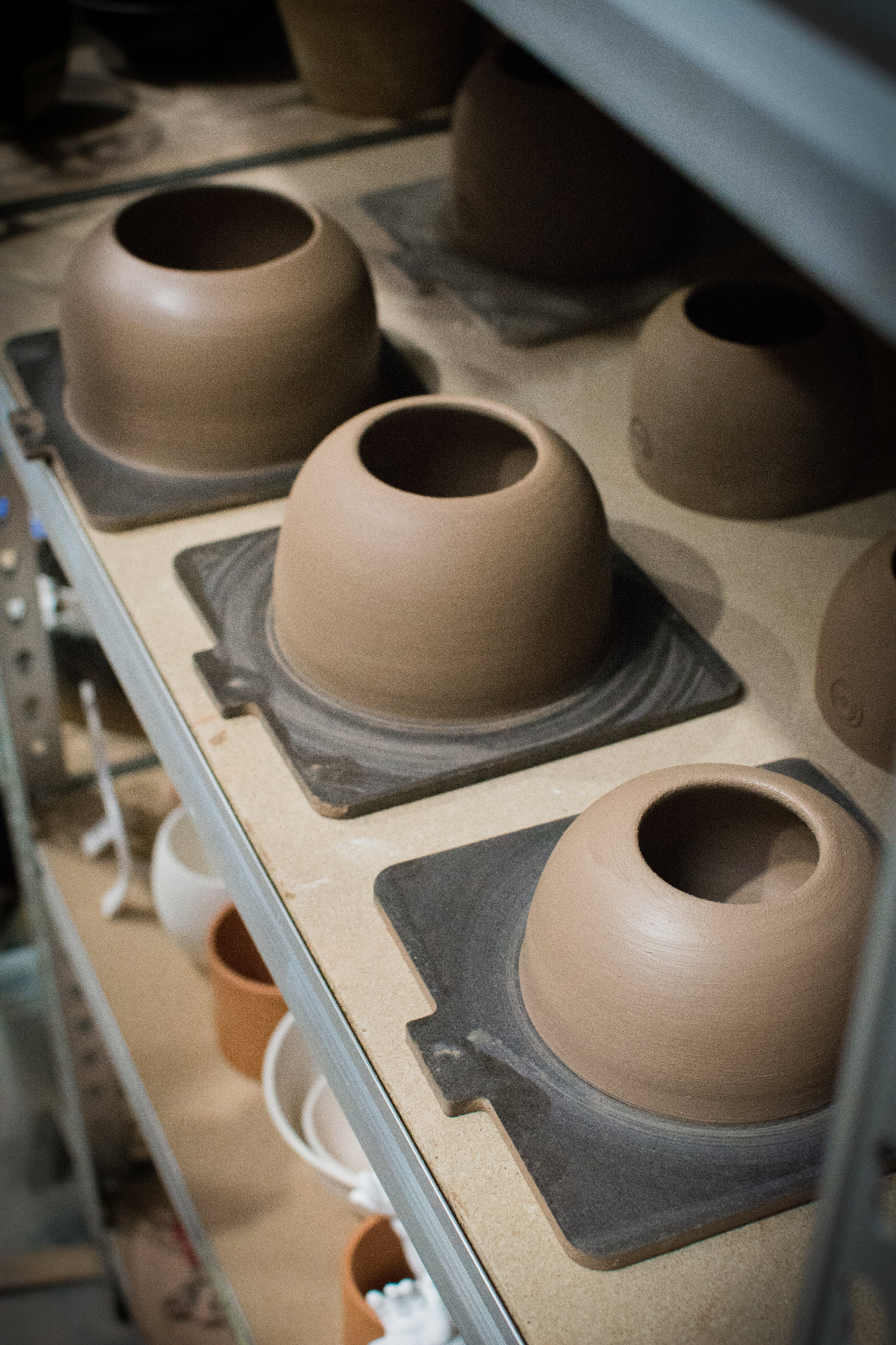 Freshly thrown clay vessels resting on bats on the studio shelving